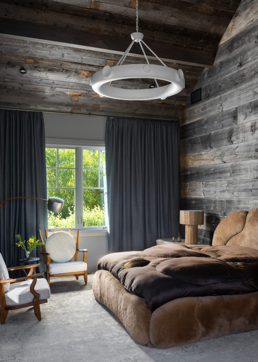 Fuzzy brown upholstered bed by Rogan Gregory in a primary bedroom clad in gray-washed barn siding in a ranch house with interiors designed by Valerie Peña in Jackson Hole Wyoming