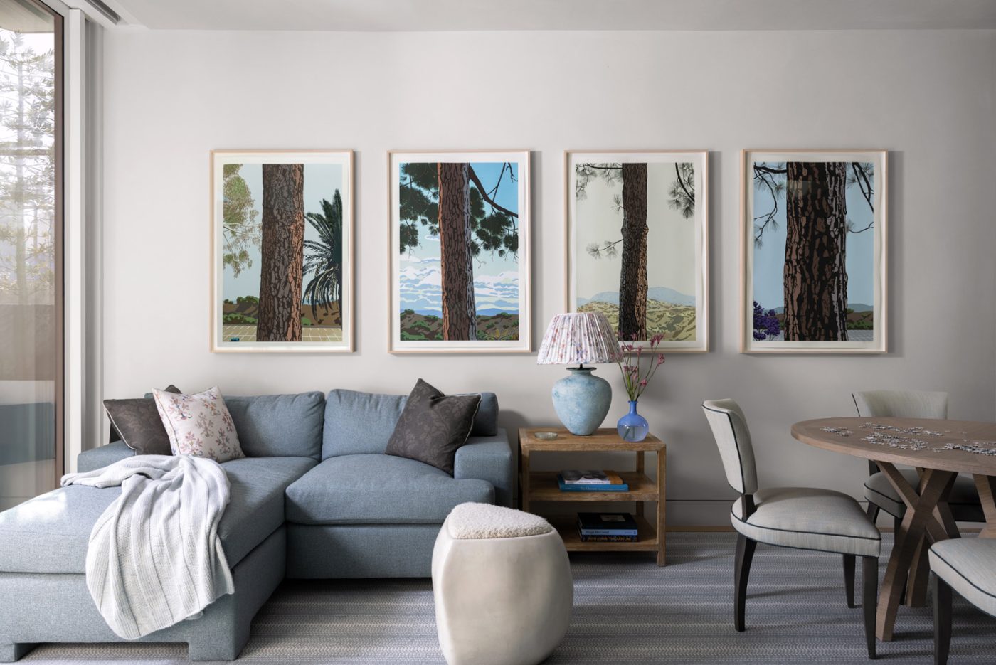 Family room of a San Francisco row house designed by Marea Clark featuring a a suite of silkscreen prints by artist Jake Longstreth lining the wall above a sectional sofa. The oak side table, sourced from Woodbridge, is topped by a mid-century glass lamp from Tarquin Bilgen.