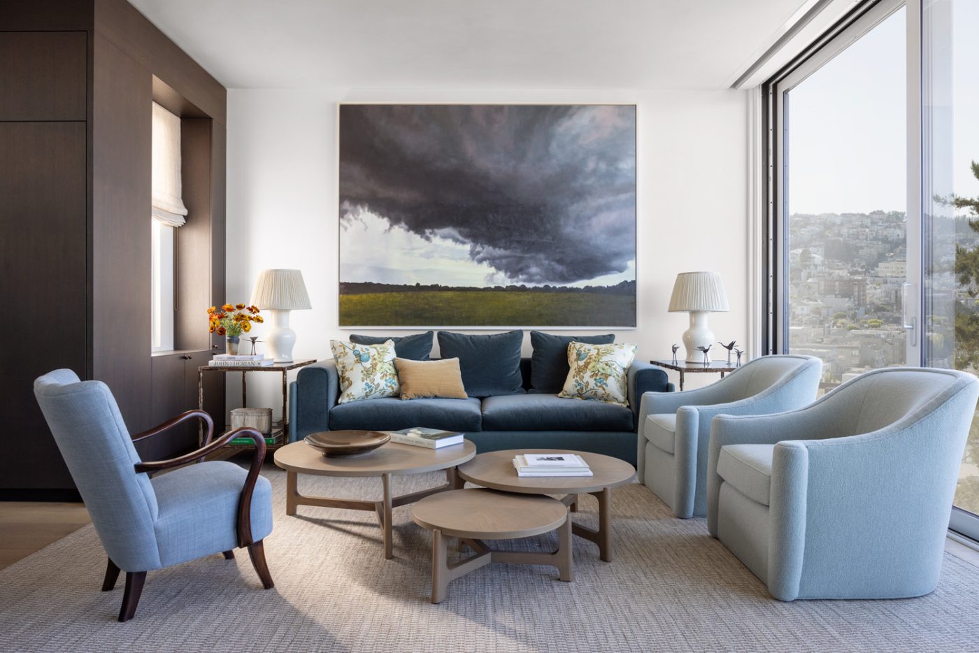 Living room of a San Francisco row house designed by Marea Clark featuring a sofa from A. Rudin, a set of circular oak coffee tables of varying heights and a landscape painting by April Gornik