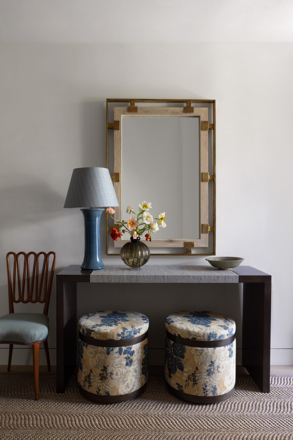 Foyer of a San Francisco row house designed by Marea Clark featuring an oak-and-brass mirror over waterfall console table with a pair of round ottomans covered underneath