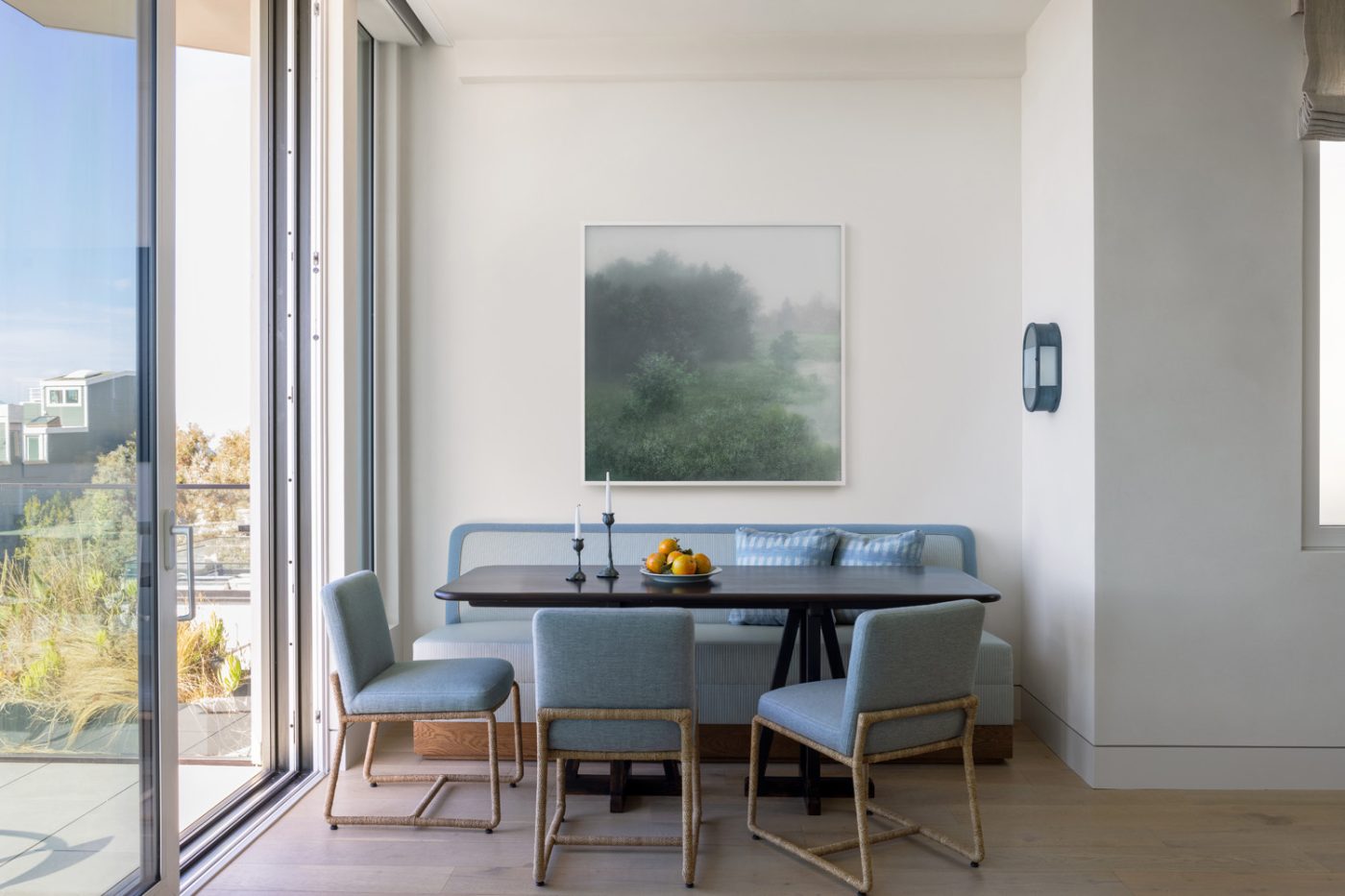Breakfast nook of a San Francisco row house designed by Marea Clark featuring chairs by Robert Kime, a custom oak table, a vintage sconce from Urban Electric and artwork by Kibong Rhee
