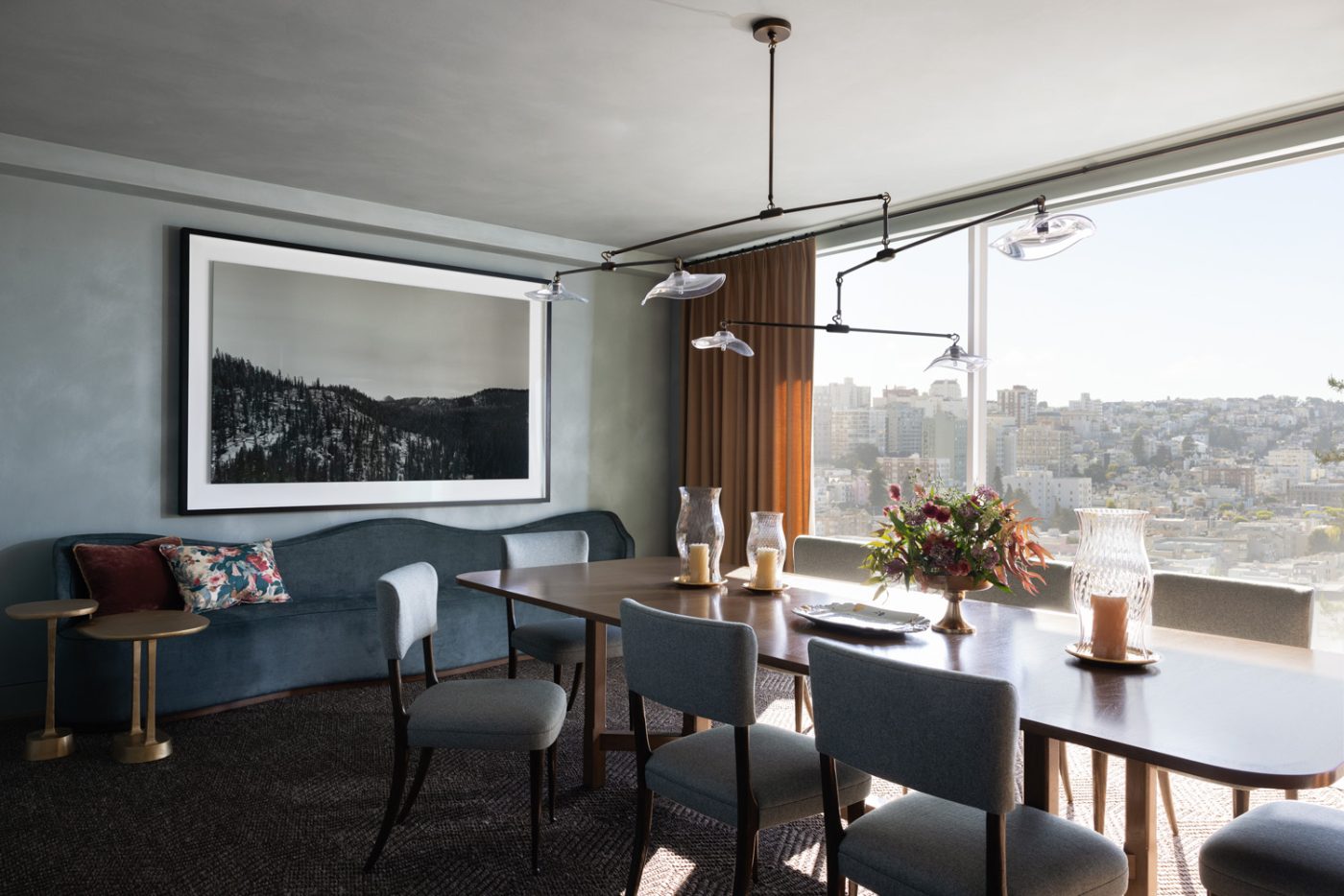 Dining room of a San Francisco row house designed by Marea Clark featuring oak dining chairs at a walnut table, a custom curving backed banquette and an oxidized-brass-and-crystal ceiling light plus art by British photographer Richard Learoyd.