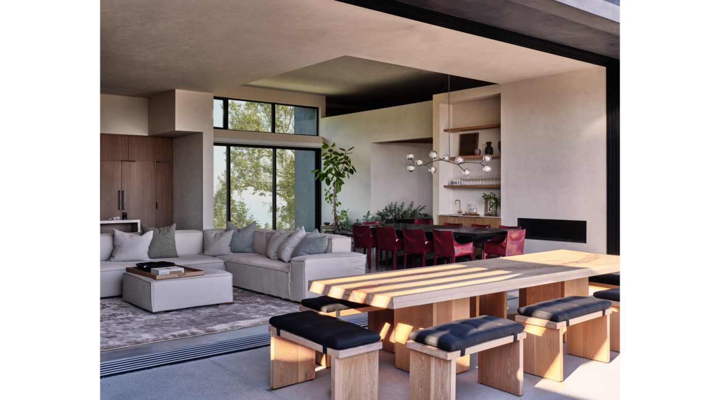 Terrace of Malibu California home of NFL player Baltimore Ravens Ronnie Stanley designed by Sarah Solis featuring a custom teak table surrounded by cushioned stools. Beyond, in the great room, is a Living Divani sectional sofa.