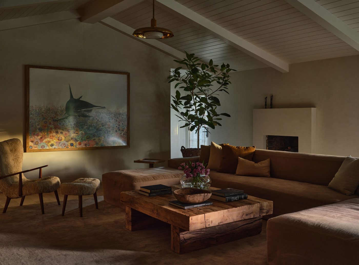 Family room of Malibu California home of interior designer Sarah Solis featuring a Galerie Solis Commune sectional sofa, a Madsen 
Schubell Pragh chair and ottoman from the 1960s and an antique French limestone mantel. The artwork is by Sage Vaughn.