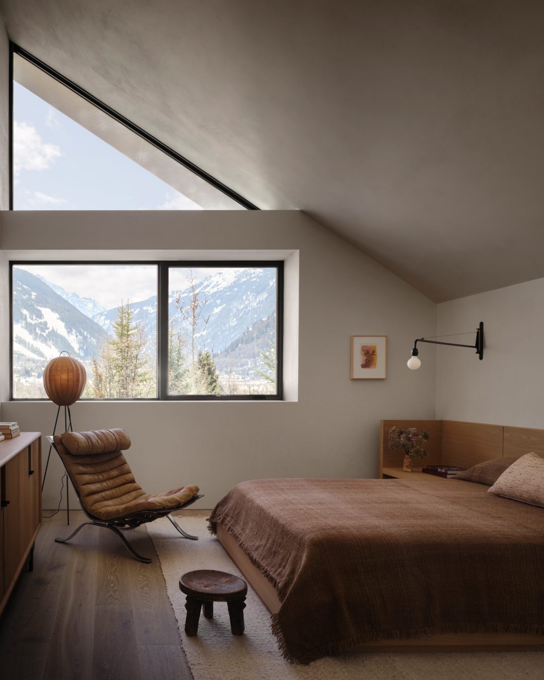 primary bedroom of a house designed by Vanessa Alexander in Aspen, Colorado, featuring a bed upholstered in a Rose Uniacke fabric, contemporary nightstands and a dresser from Luteca. The art over the bed is by Stefan Simchowitz.
