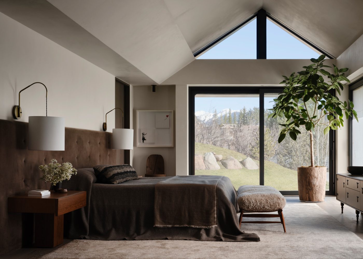 primary bedroom of a house designed by Vanessa Alexander in Aspen, Colorado, featuring a custom headboard and bed upholstered in a Rose Uniacke cotton velvet, custom swing-arm brass sconces, a contemporary bench and a BDDW dresser.