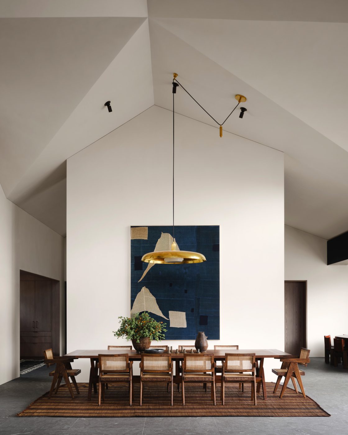 dining room of a house designed by Vanessa Alexander in Aspen, Colorado, featuring Pierre Jeanneret chairs at a long rectangular wood table under a gold-toned disk-like pendant light