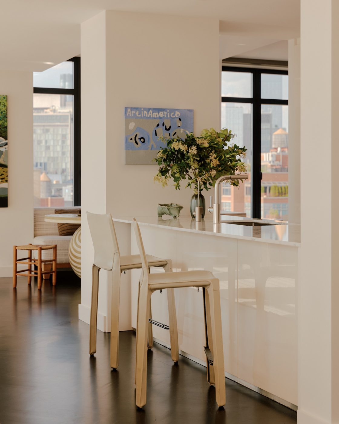Kitchen with Cassina counter stool across from sink and view to casual dining area beyond in nearly all white minimalist loft apartment in New York's West Village  designed by Clive Lonstein. Marlon Mullen painting on column