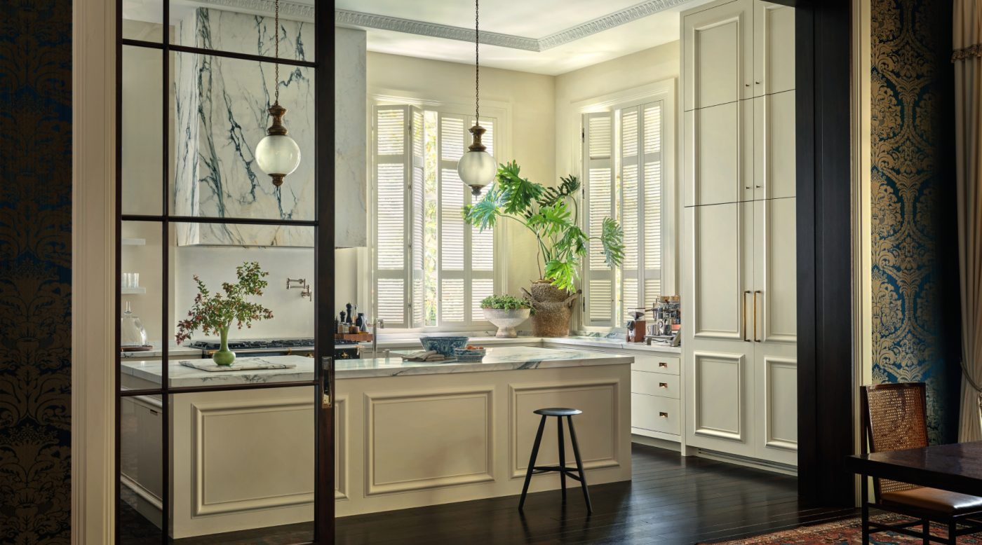 View through glass doors from dark dining room to light pale white kitchen in Edwardian house San Francisco's Pacific Heights with interiors by Brittany Giannone's ABD STUDIO