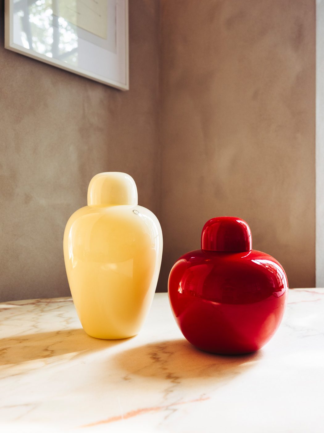 Two Murano-glass vessels — one pale ivory colored the other deep red and both by Tobia Scarpa for Venini — seen on a marble surface at the Italian Collector, the Florence Italy shop of antiques dealer Bec Astley Clarke