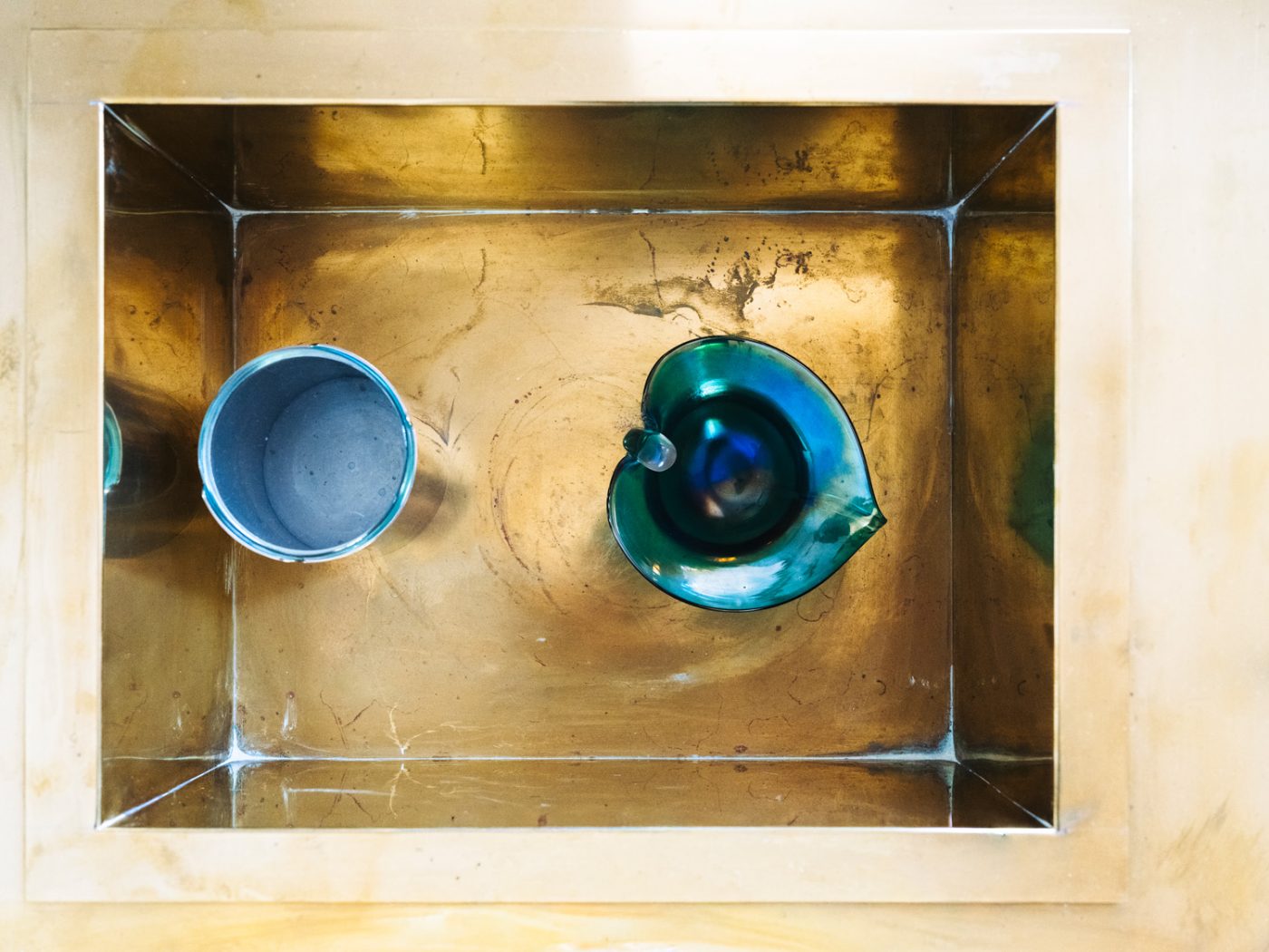An aquamarine-colored Murano glass leaf-shaped cup by Alfredo Barbini and a silvery blue cylindrical vessel seen from above in the reservoire of a brass Gabriella Crispi coffee table at the Italian Collector, the Florence Italy shop of antiques dealer Bec Astley Clarke