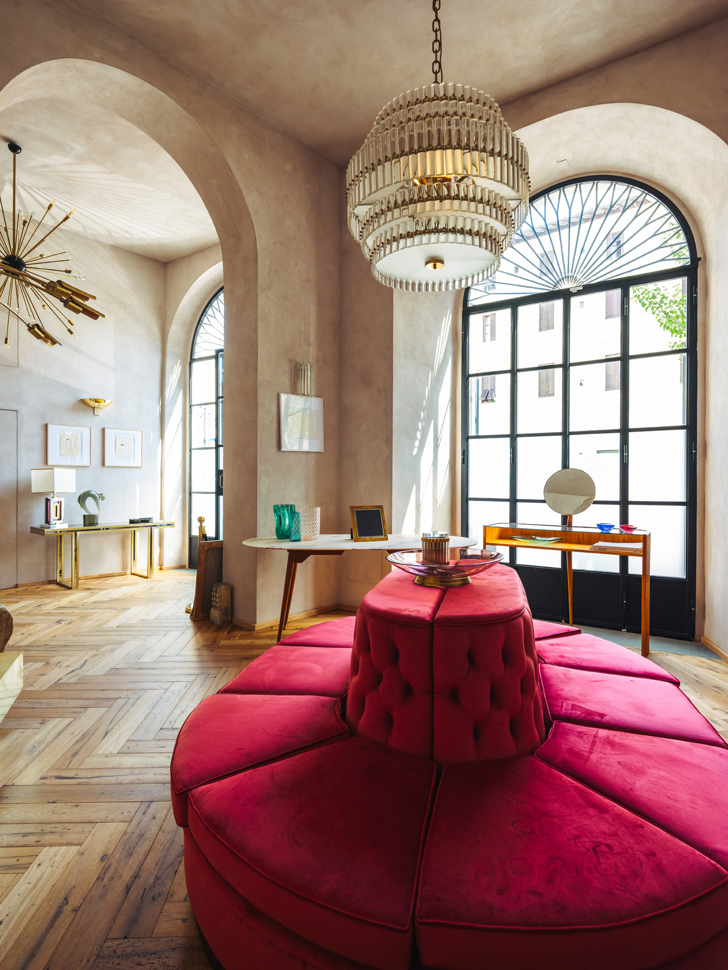The main rooms of Italian Collector, the Florence Italy shop of antiques dealer Bec Astley Clarke, filled with mostly mid-century-modern Italian antiques, including a bright pink circular sofa and large crystal chandelier