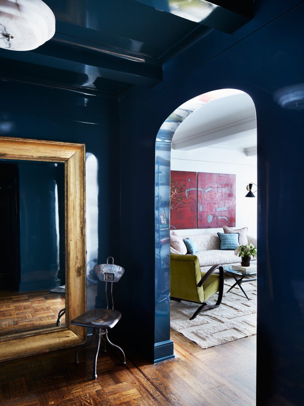 A stylish interior design featuring a high-gloss, deep blue entrance hall opening into a living area, in an apartment on New York's Upper East Side designed by Erik Gensler