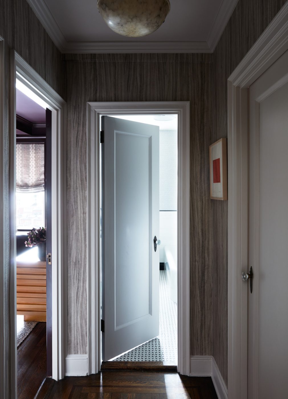 Hallway in an apartment on New York's Upper East Side designed by Erik Gensler featuring wood-grain-like wallpaper and alabaster pendant lamp