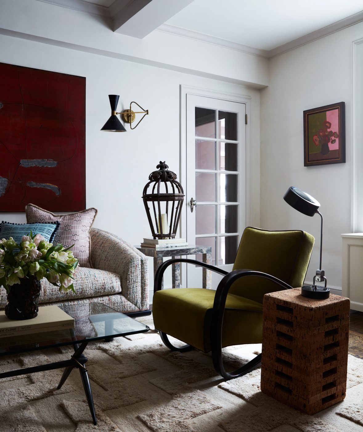Living room of an apartment on New York's Upper East Side designed by Erik Gensler featuring Jindřich Halabala armchair, trestle coffee table from Bourgeois Boheme Atelier, cork side table, fluffy beige carpet from Nordic Knots, and a swing-arm sconce beside a red two-part painting