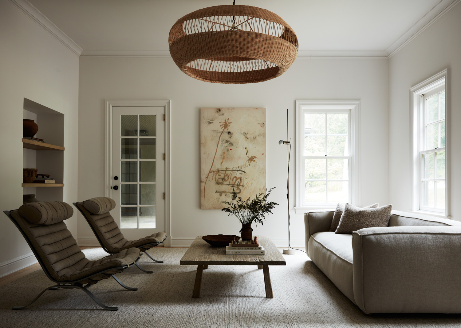 Den in Upstate New York home designed by Maggie Smith with vintage Arne Norell chairs and a chunky contemporary sofa, as well as a reclaimed-wood coffee table by Dos GalloS Studio. The floor lamp is by Tito Agnoli, and the art is by Armando Mesías