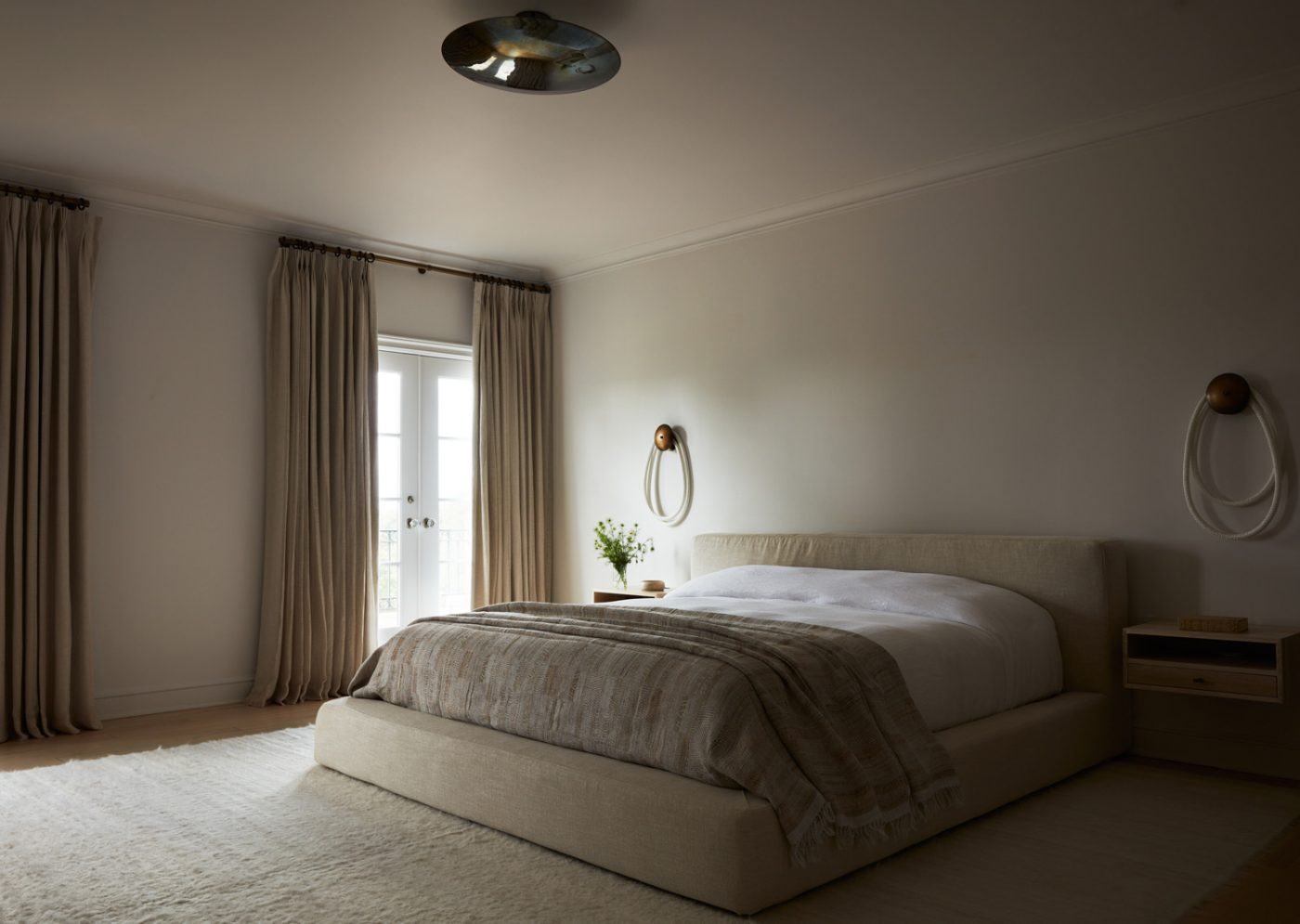 Primary bedroom in Upstate New York home designed by Maggie Smith with rope-light wall sconces and custom floating nightstands flanking an upholstered bed