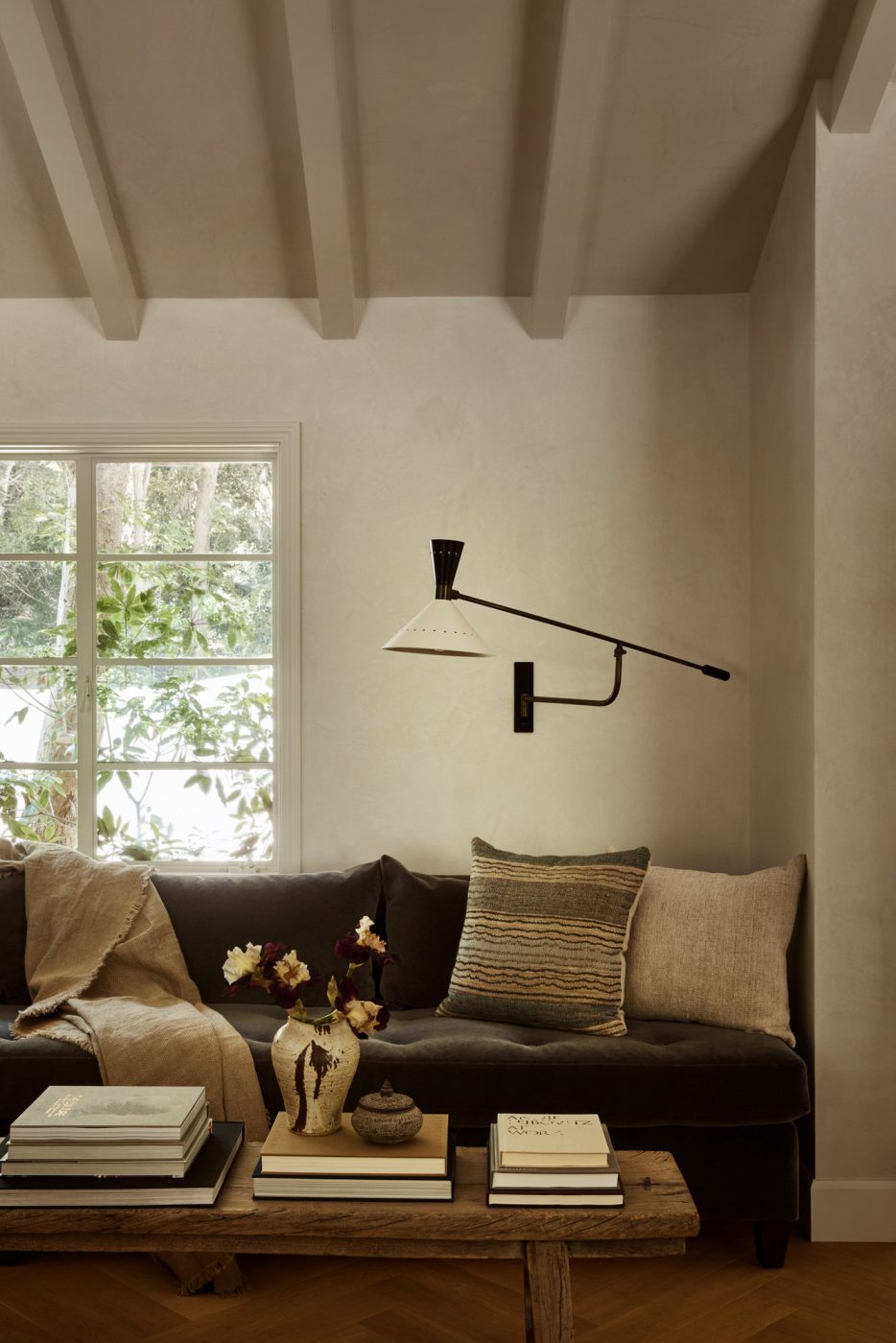 Area near front door in living room of Beverly Hills home designed by Maggie Smith with a vintage Hans-Agne Jakobsson sconce on the wall above a mohair-upholstered tufted settee.