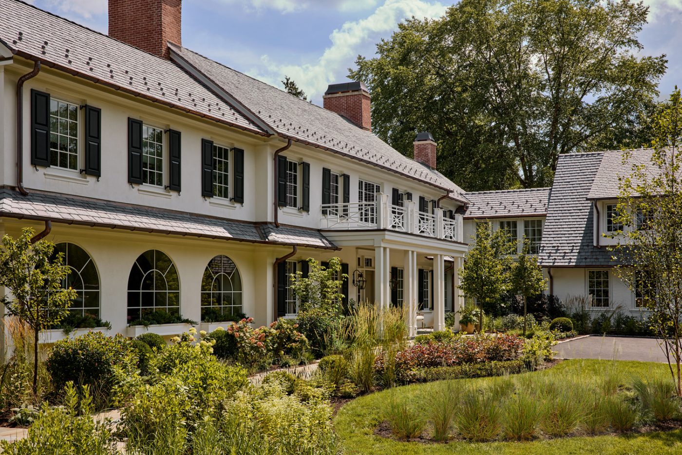 White exterior with paned windows and black shingles of a recently finished vintage Colonial-style home redesigned by Autumn Oser and Andre Golsorkhi, partners in the design firm Haldon House