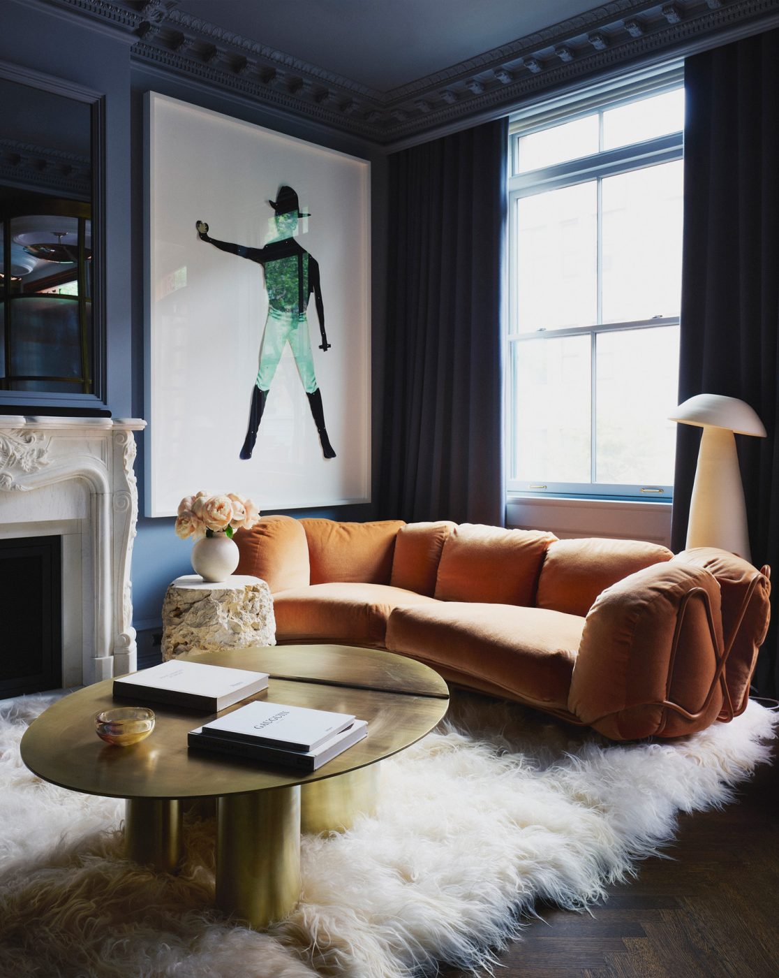 Goat fur rug, orange postmodern sofa, contemporary steel coffee table and traditional marble white fireplace in Dark blue walled living room in Harlem townhouse designed by Crystal Sinclair