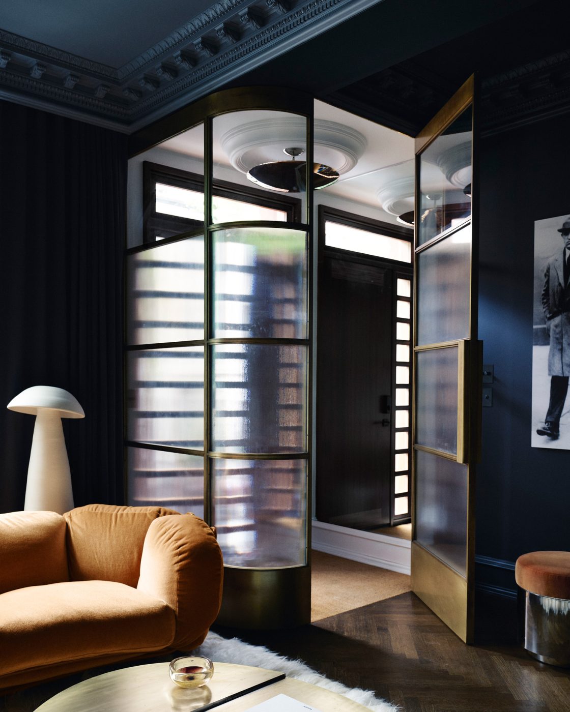 Dark blue walled living room and glass and brass vestibule in Harlem townhouse designed by Crystal Sinclair