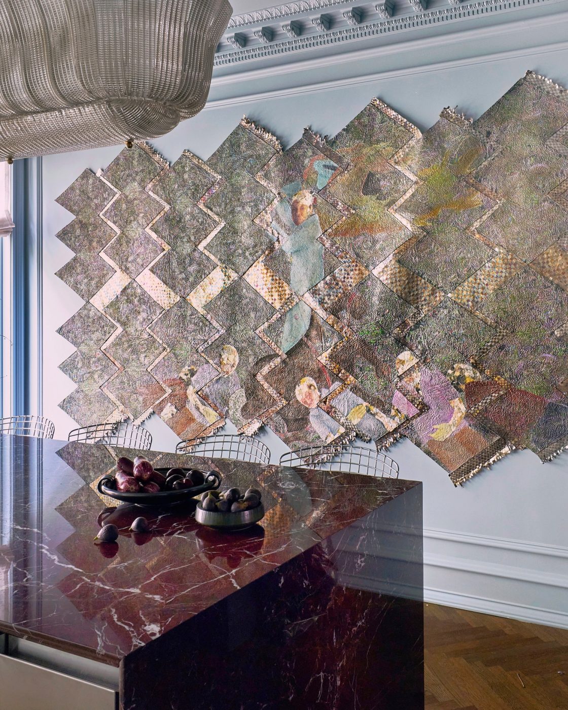 Polished red marble island in pale blue-gray kitchen with elaborate moldings, Murano chandelier and herringbone floors in a Harlem townhouse design by Crystal Sinclair