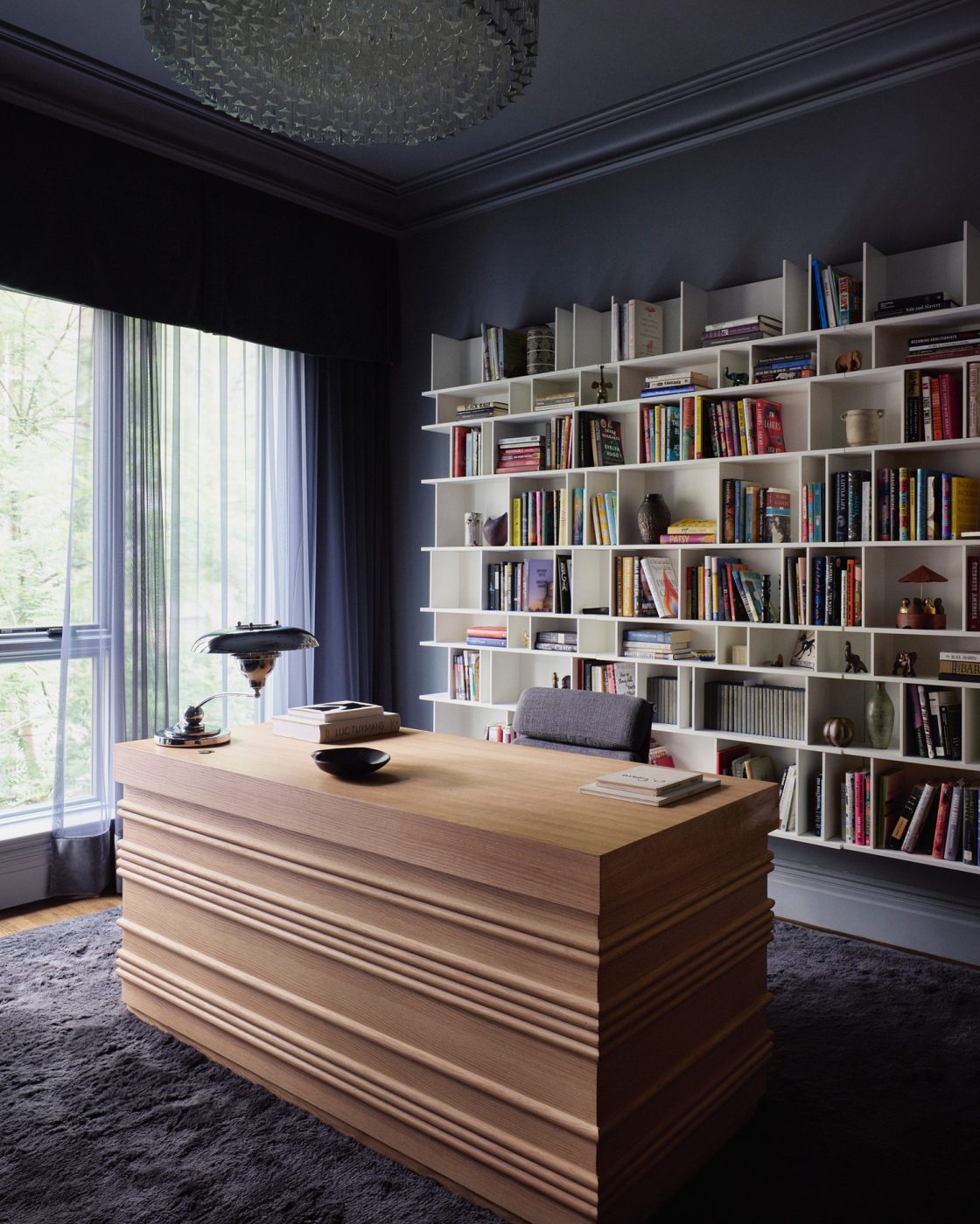 White bookshelves behind a natural wood desk on a dark gray shag carpet in the gray-walled office in a Harlem townhouse designed by Crystal Sinclair