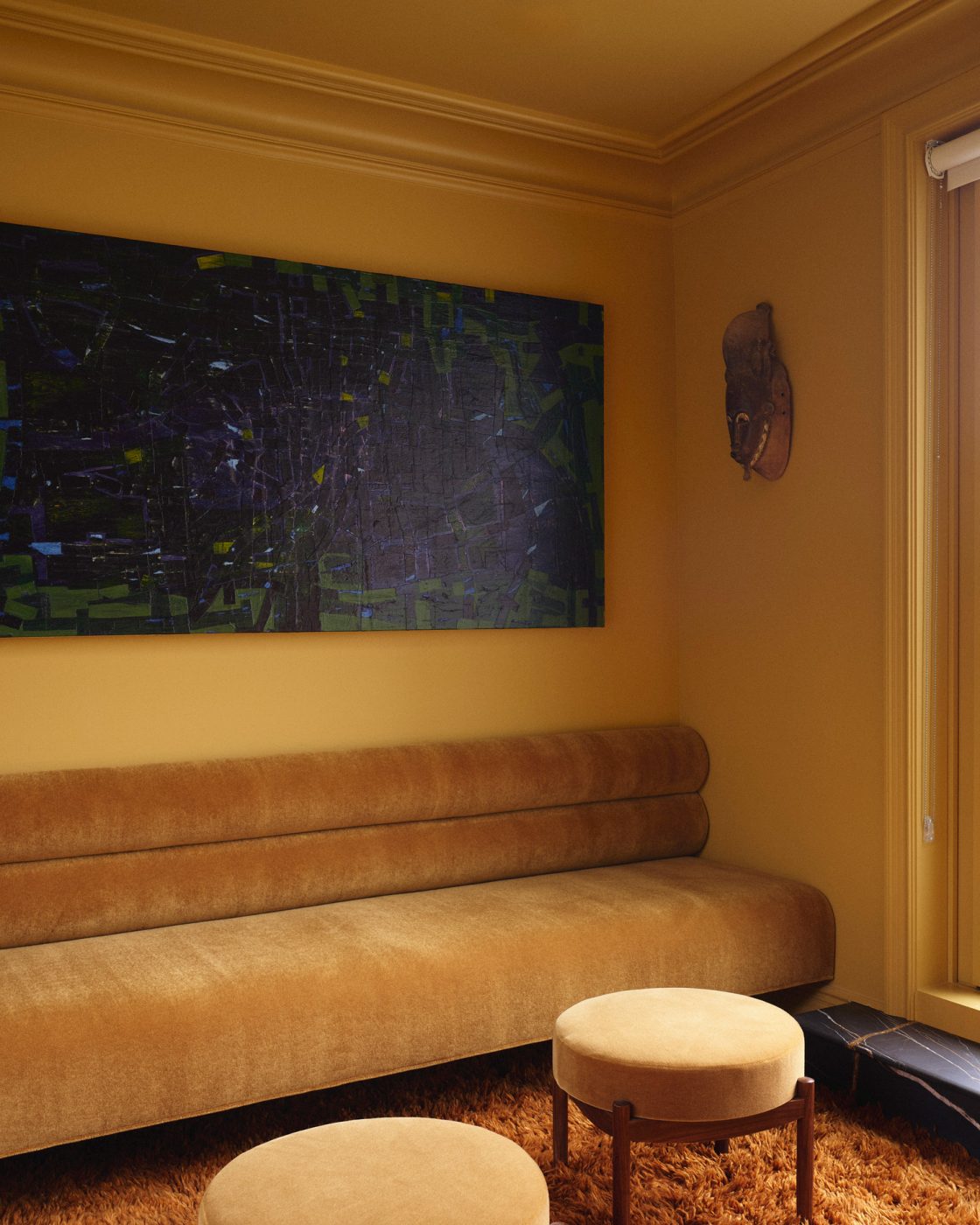Allover golden yellow seating area with built in banquette and matching upholstered stools atop a deep orange shag carpet on top floor of a Harlem townhouse designed by Crystal Sinclair