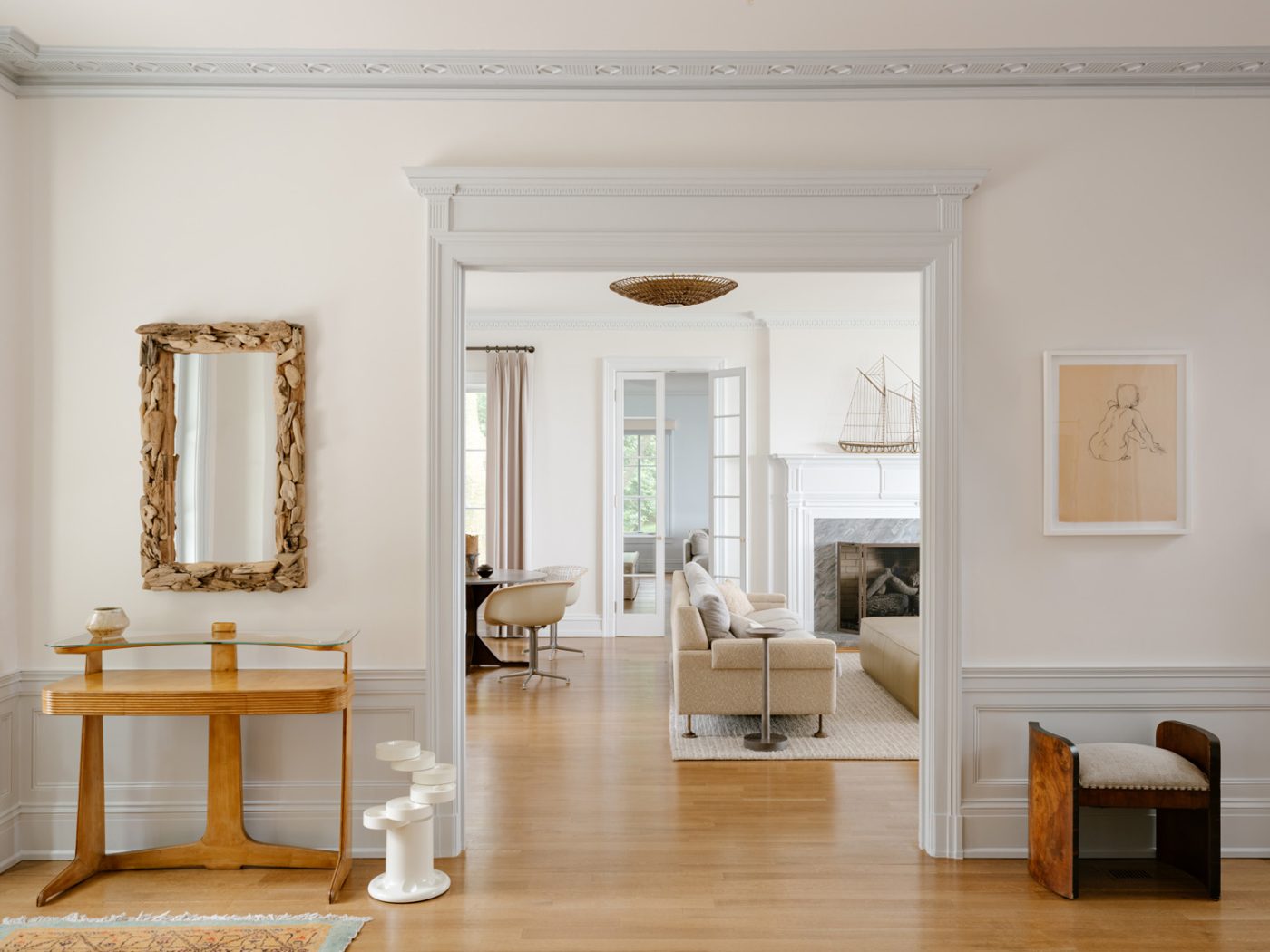 Vintage wooden pieces in the minimally furnished pale neutrally hued entry with view to living room and den of a of a Long Island home with interiors by studio Evan Edward designers Michael Edward Moirano and Josh Evan Goldfarb