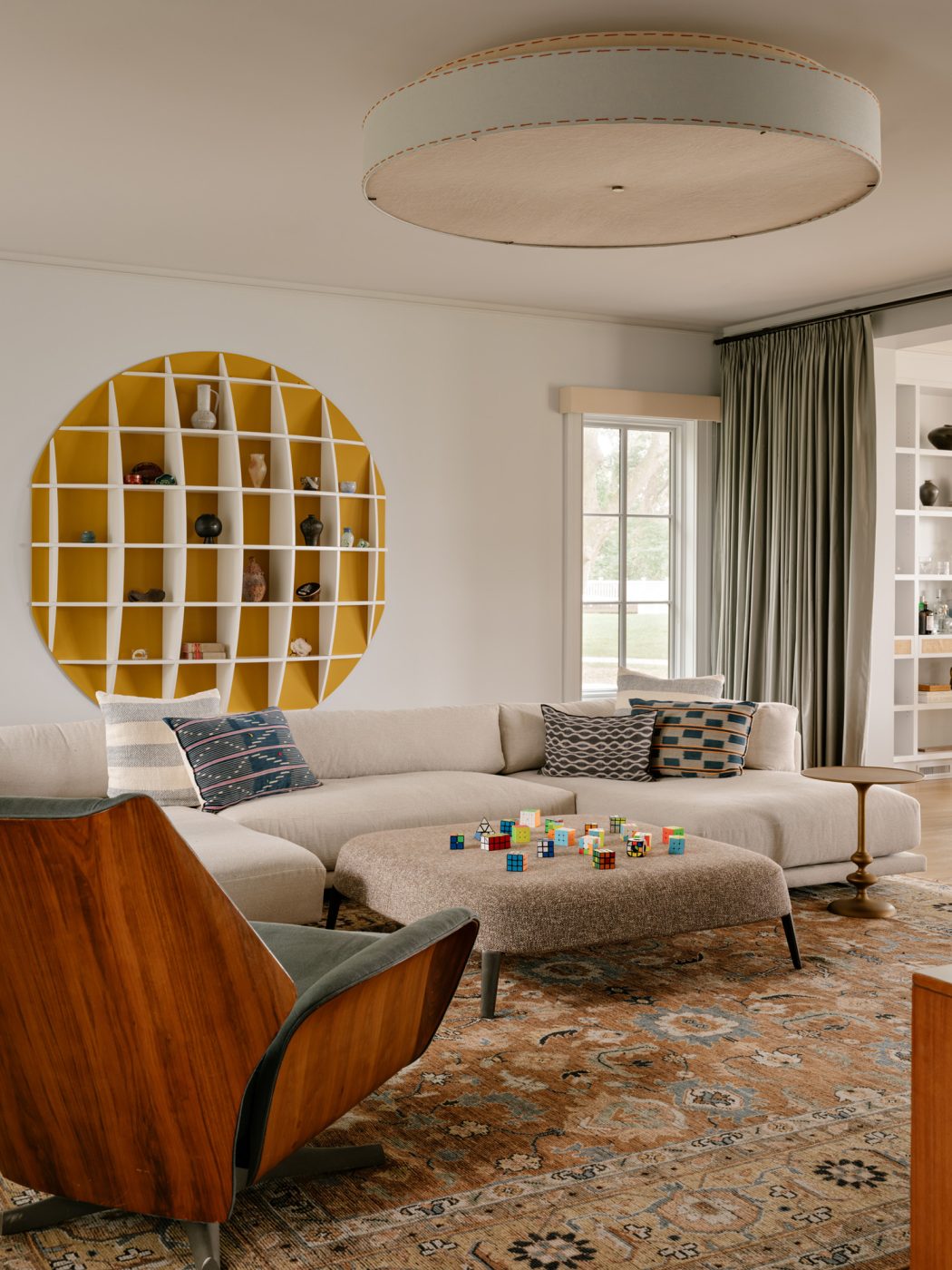 A circular, wall-mounted Manfredo Massironi for Nikol International bookshelf, a contemporary U-shaped sectional sofa, 1960s lounge chair by Raymond Loewy, and ottoman by Antonio Citterio for Maxalto in the TV room of a Long Island home with interiors by studio Evan Edward designers Michael Edward Moirano and Josh Evan Goldfarb