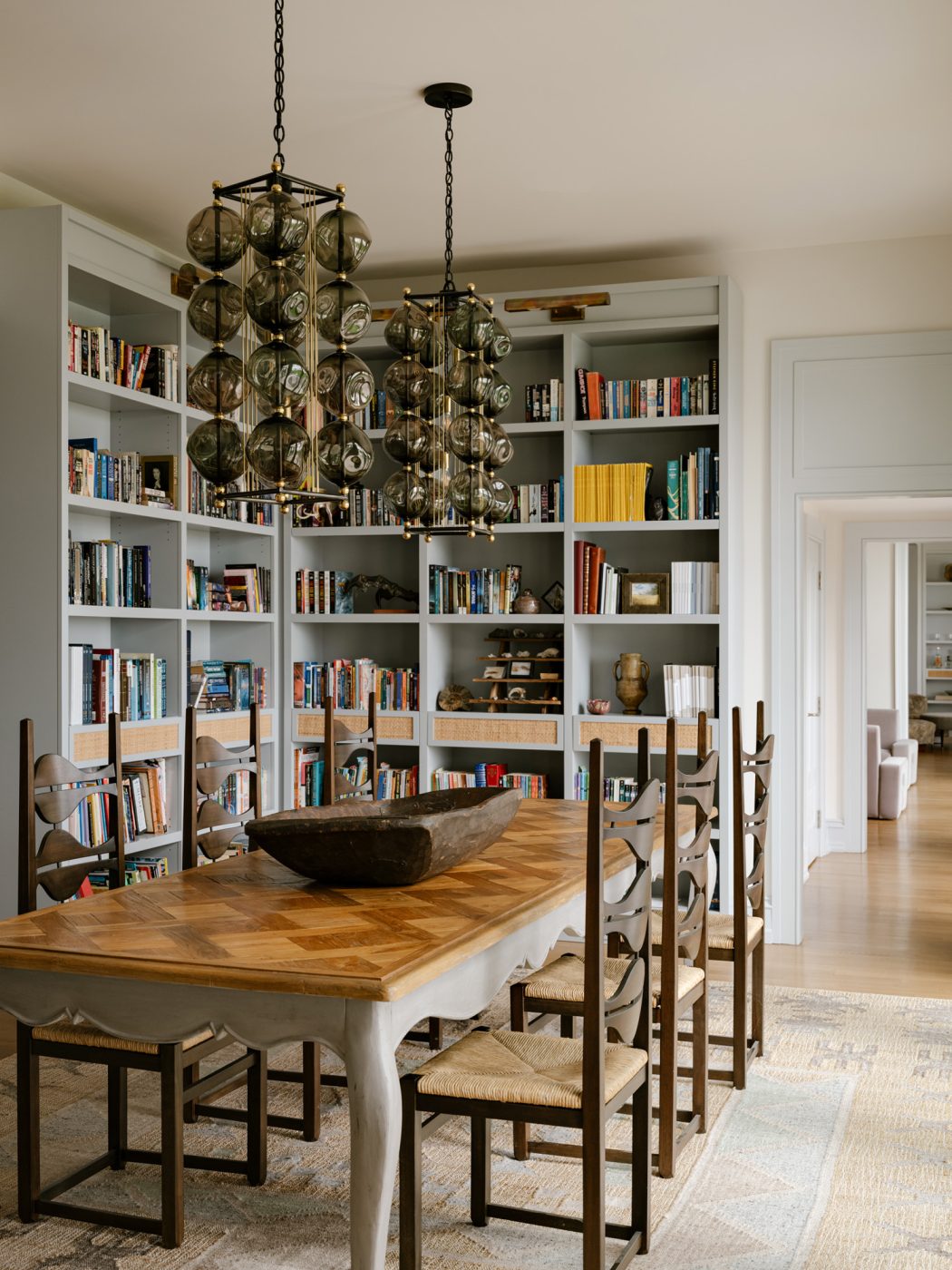 Jordi Vilanova i Bosch chairs from the 1960s surrounding a a French Provincial–style table with pendant lights from Bourgeois Boheme hanging above in the bookshelf-lined, library-like dining room of a Long Island home with interiors by studio Evan Edward designers Michael Edward Moirano and Josh Evan Goldfarb