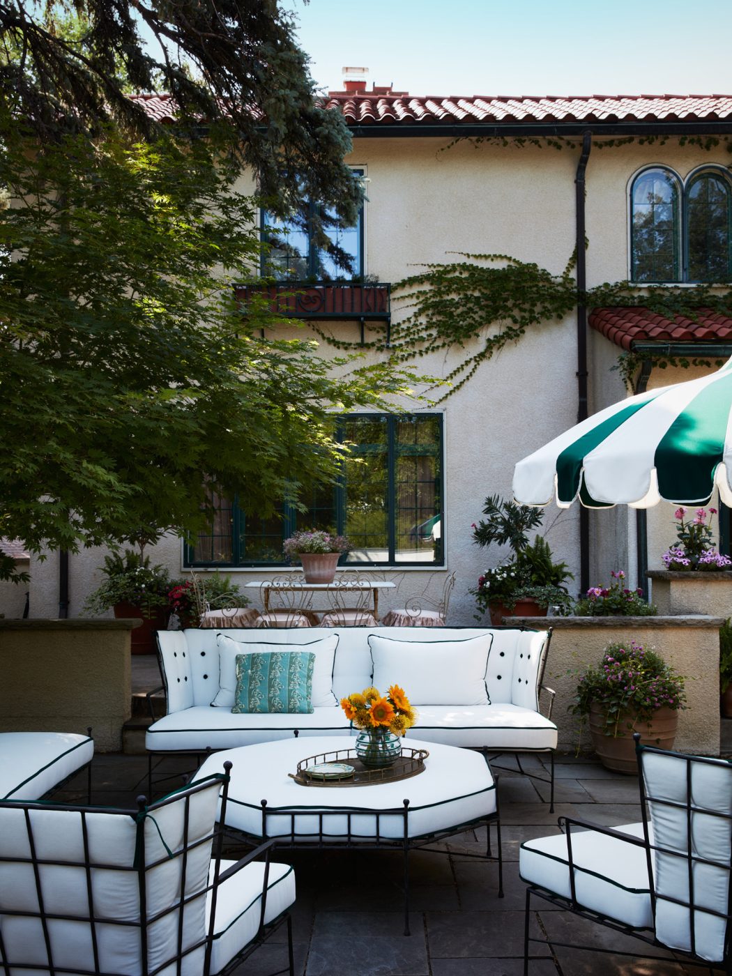 Black metal-framed outdoor furniture with white button-tufted cushions in the patio garden of a Mediterranean-style house in Minneapolis, Minnesota