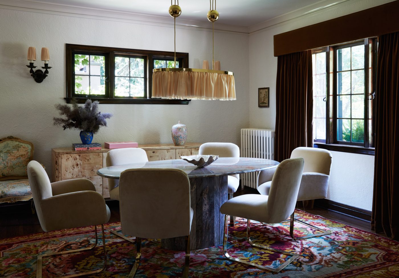 A vintage stone table surrounded by mid-century modern chairs under a Jugendstil brass-and-silk chandelier by Adolf Loos in the dining room of a Mediterranean-style house in Minneapolis, Minnesota