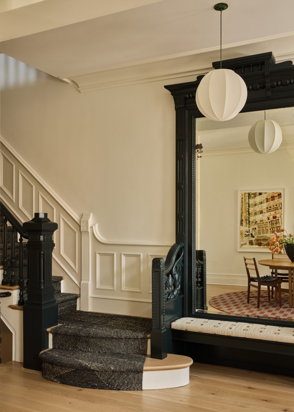 Entry hall of Prospect Heights Brooklyn brownstone renovated by the interior design firm Jesse Parris-Lamb featuring a dark green-black painted original carved wood banister and frame of large wall mirror that is reflecting the dining area