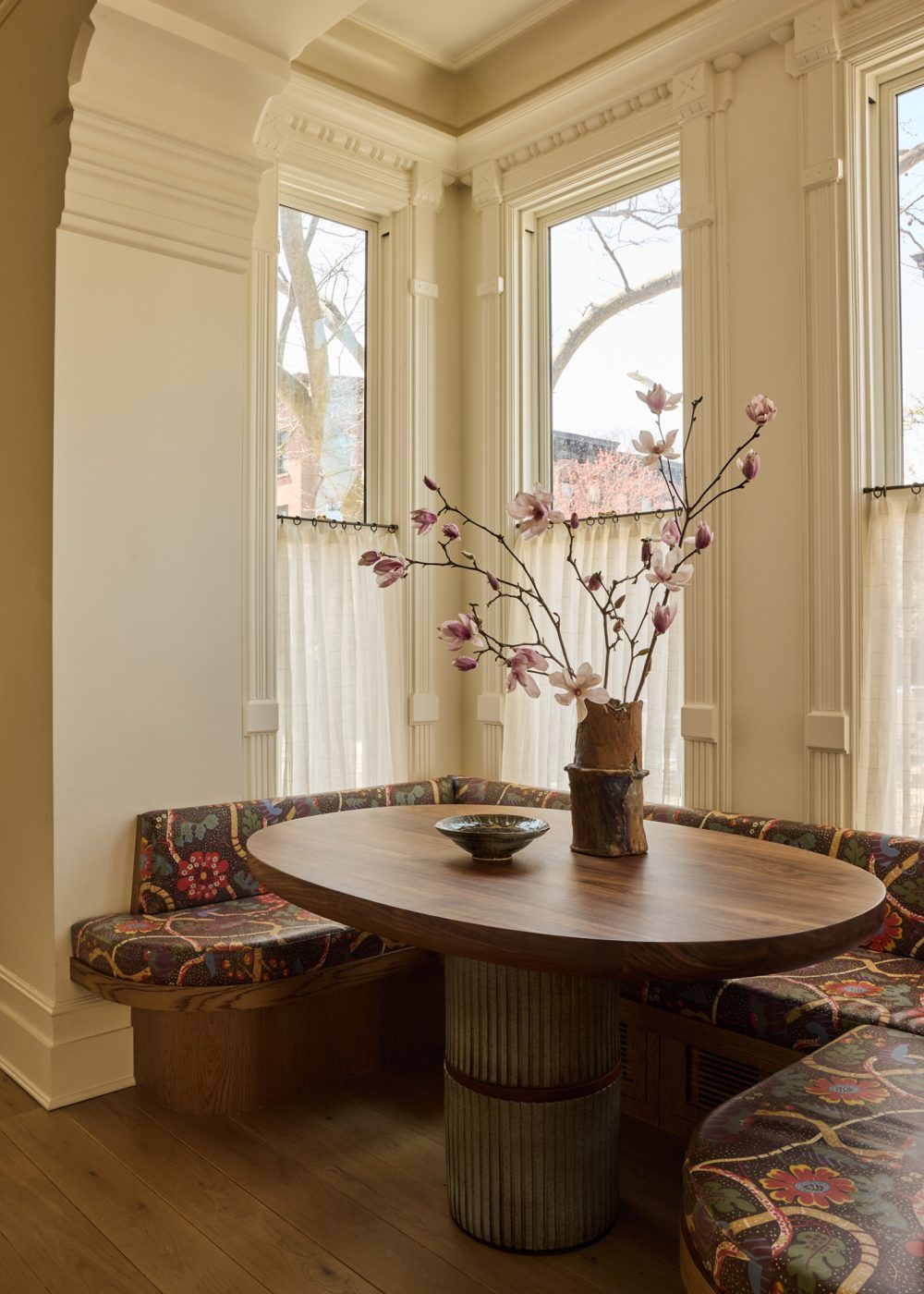 Kitchen dining nook in window bay with built in banquette upholstered in Josef Frank fabric surrounding custom table with ceramic base in Prospect Heights Brooklyn brownstone renovated by the interior design firm Jesse Parris-Lamb