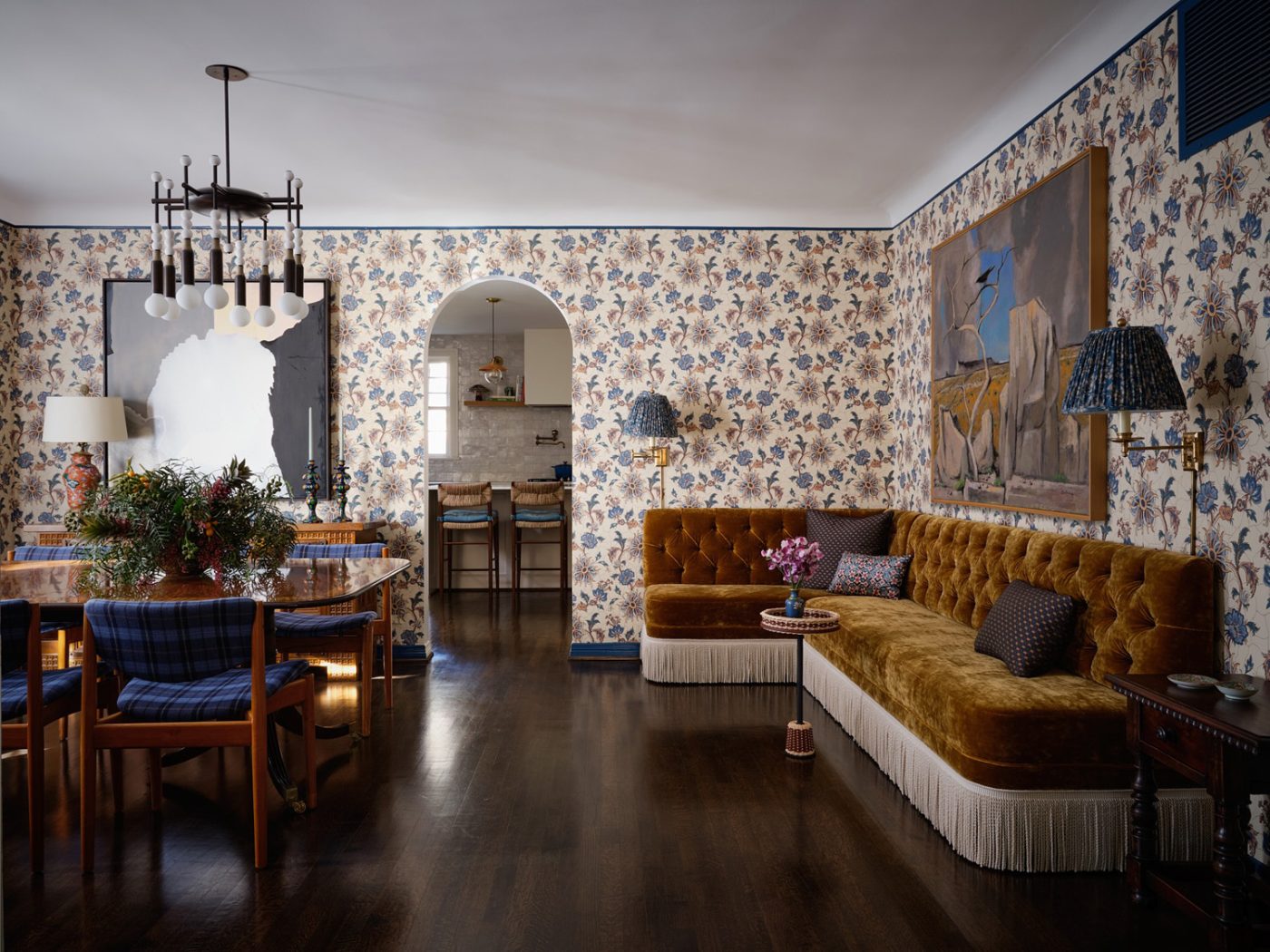 dining room with botanical wallpaper, plaid-upholsted mid-century chairs, fringed gold-tone corner banquette and contemoary art and dark floors in a Spanish Colonial house in Highland PArk Village Dallas designed by Dafna Kikuchi of Daf&Co