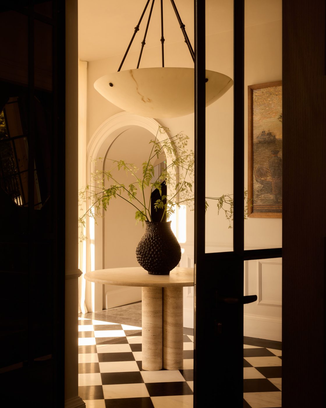 Travertine center table on black-and-white checkerboard floor in entry of 19th-century Georgian-style manor house in Irish Countryside designed by Dublin-based Róisín Lafferty