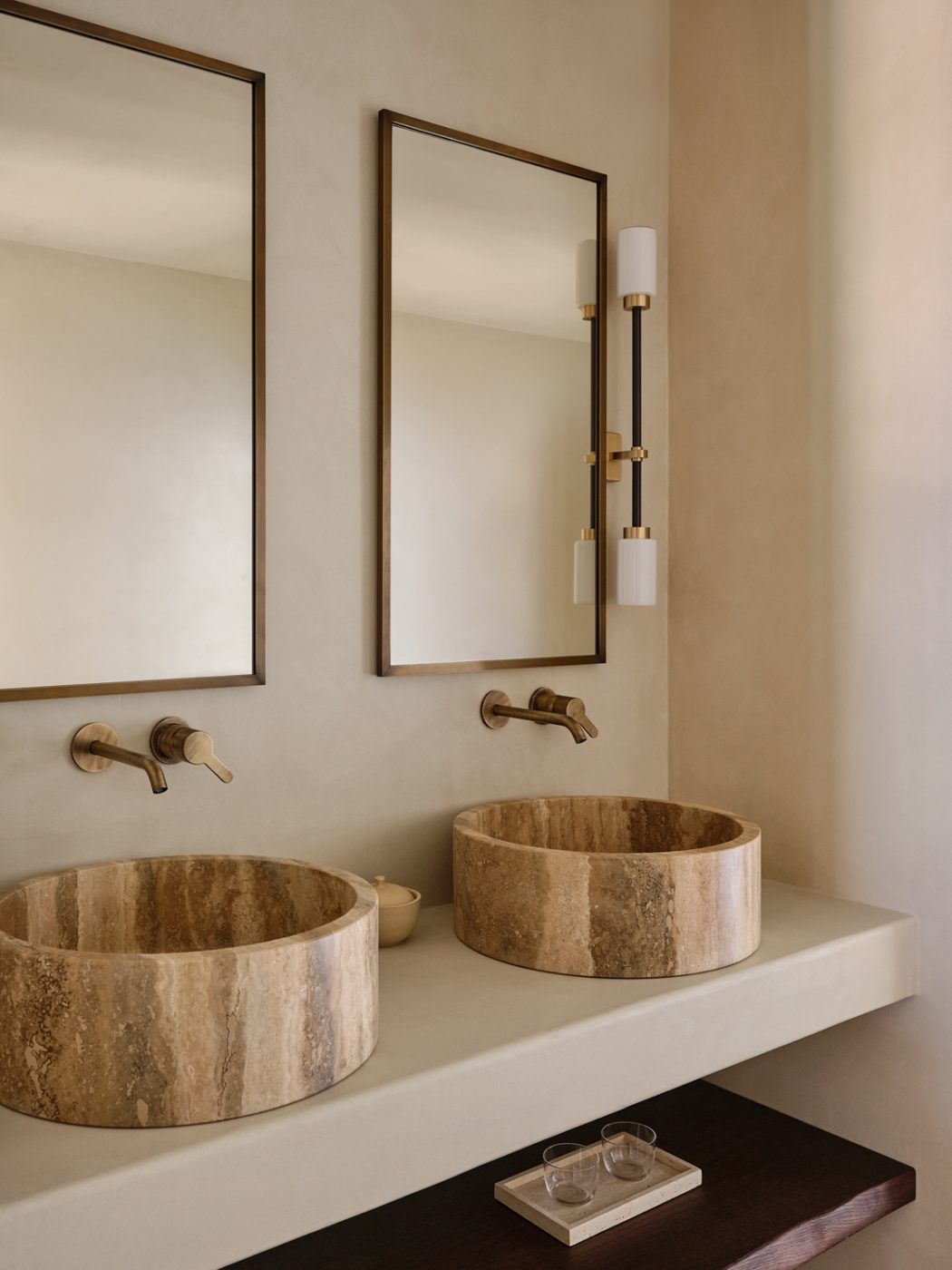 Guest bathroom with travertine countertop sinks in a Milan penthouse whose interiors are by Edo Mapelli Mozzi, founder of the design and development firm Banda.