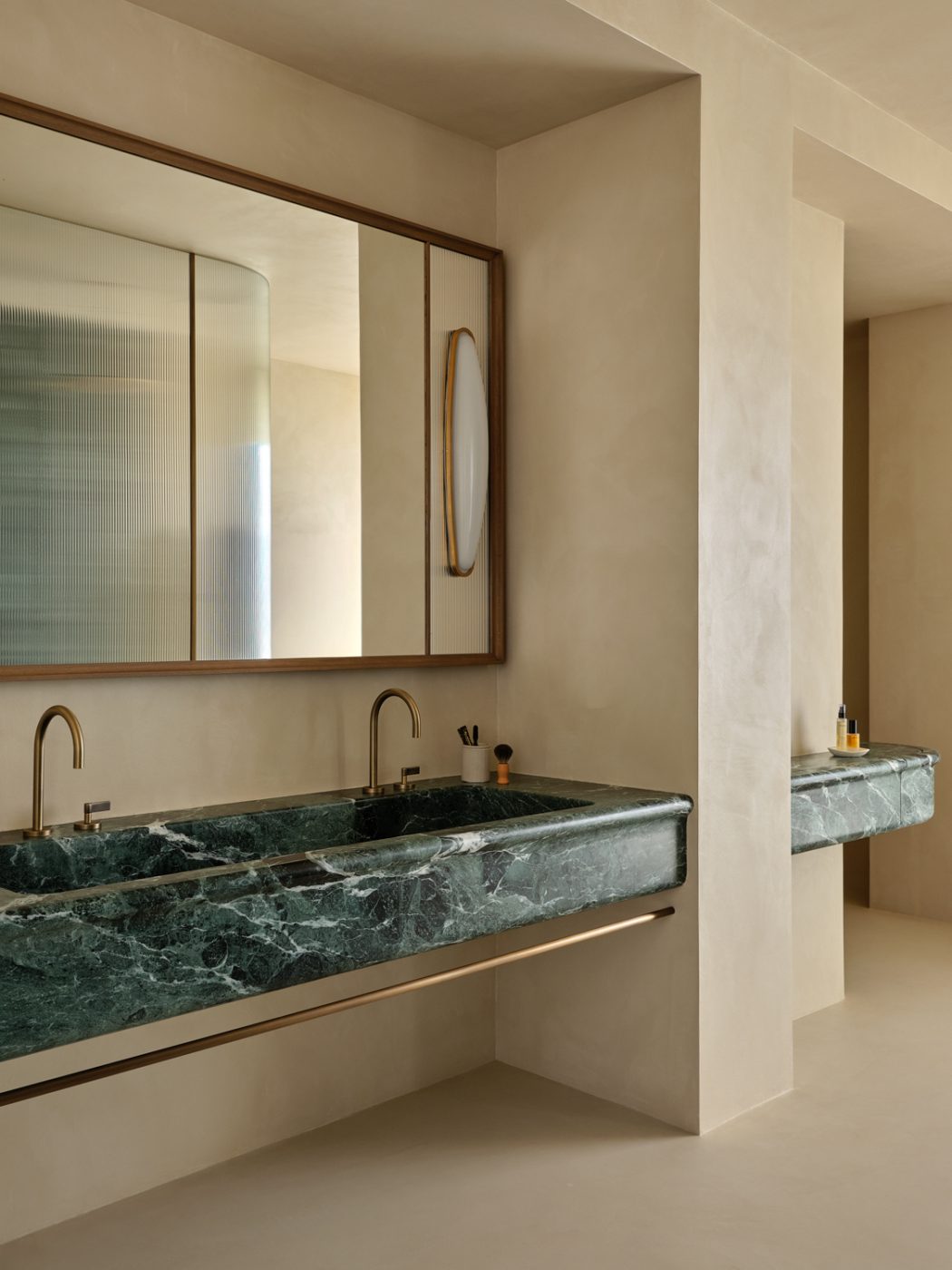 Plaster walled primary bathroom with green marble floating vanities in a Milan penthouse whose interiors are by Edo Mapelli Mozzi, founder of the design and development firm Banda.