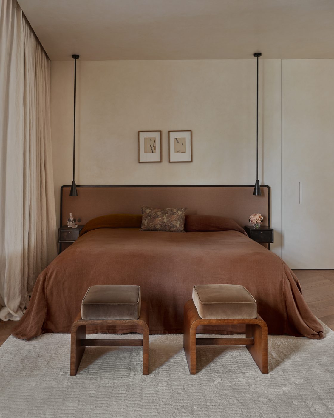 Cinammon-hued upholstered headboard and velvet cushioned stools in primary bedroom of a Milan penthouse whose interiors are by Edo Mapelli Mozzi, founder of the design and development firm Banda.
