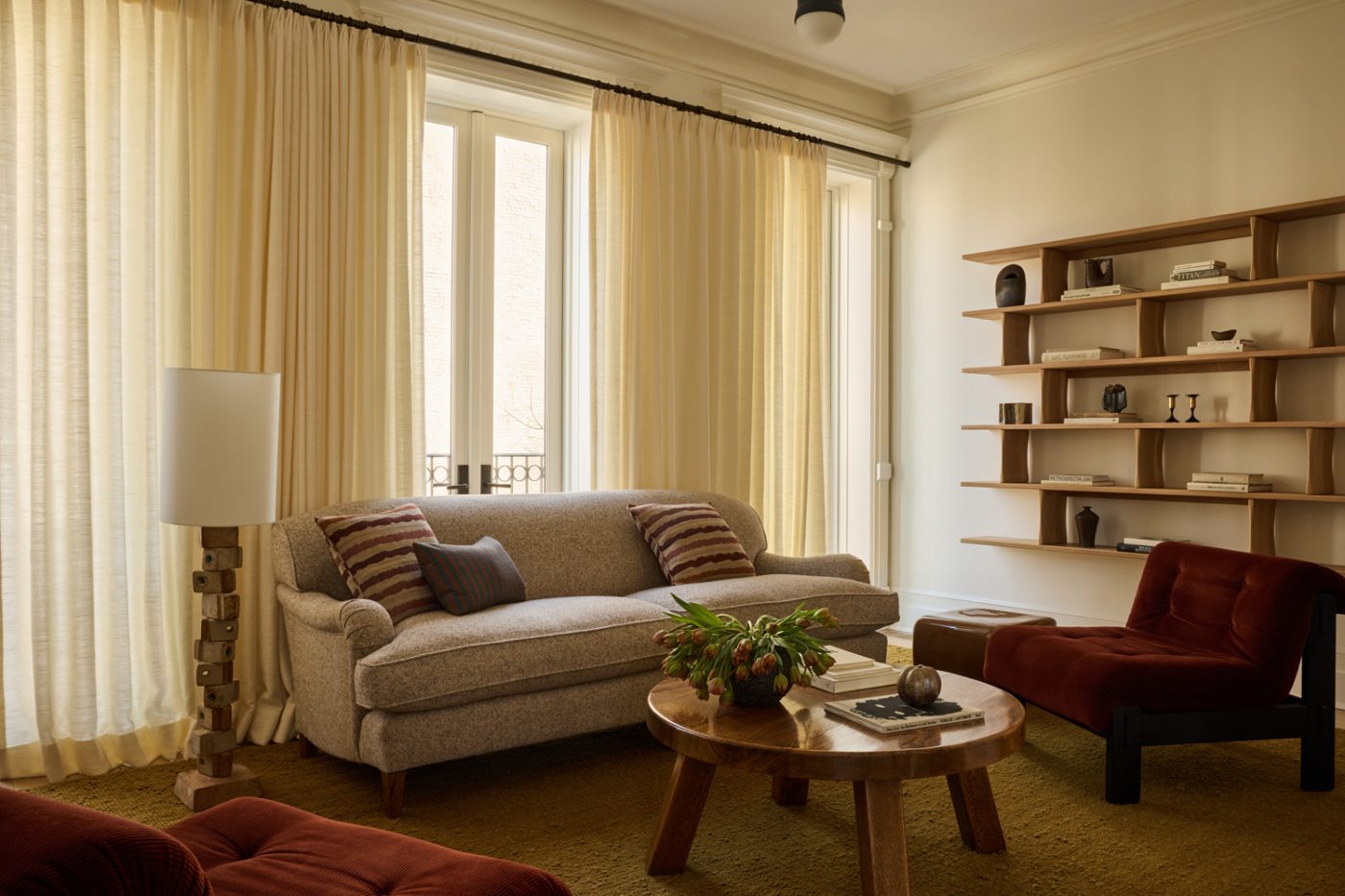 Living room with gray George Smith sofa, 1970s lounge chairs in red corduroy, round coffee table and wall mounted shelves from Richard Watson in Prospect Heights Brooklyn brownstone renovated by the interior design firm Jesse Parris-Lamb
