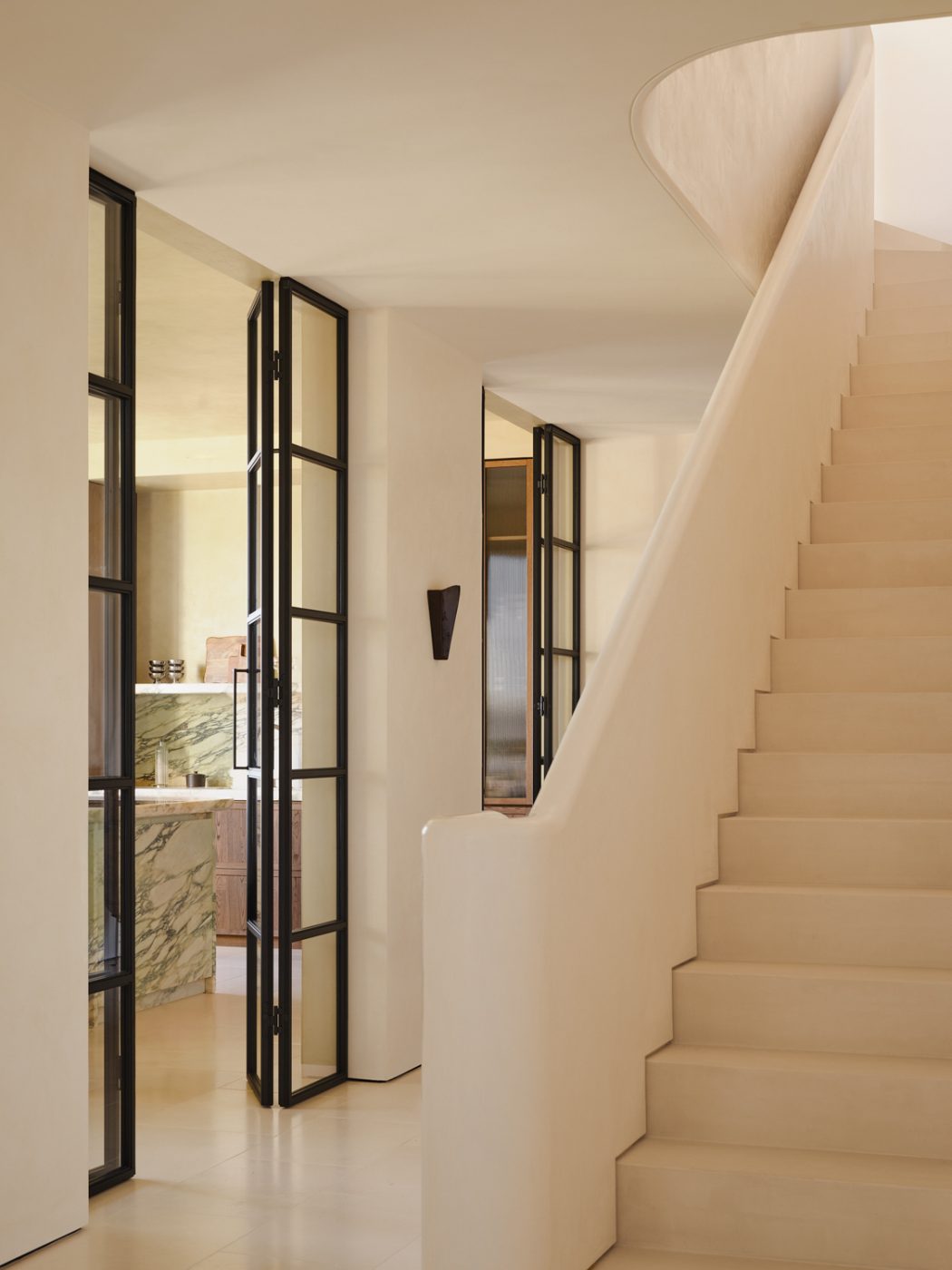 Main hall with staircase up and view to kitchen through steel-and-glass doors in a Milan penthouse whose interiors are by Edo Mapelli Mozzi, founded of the design and development firm Banda.
