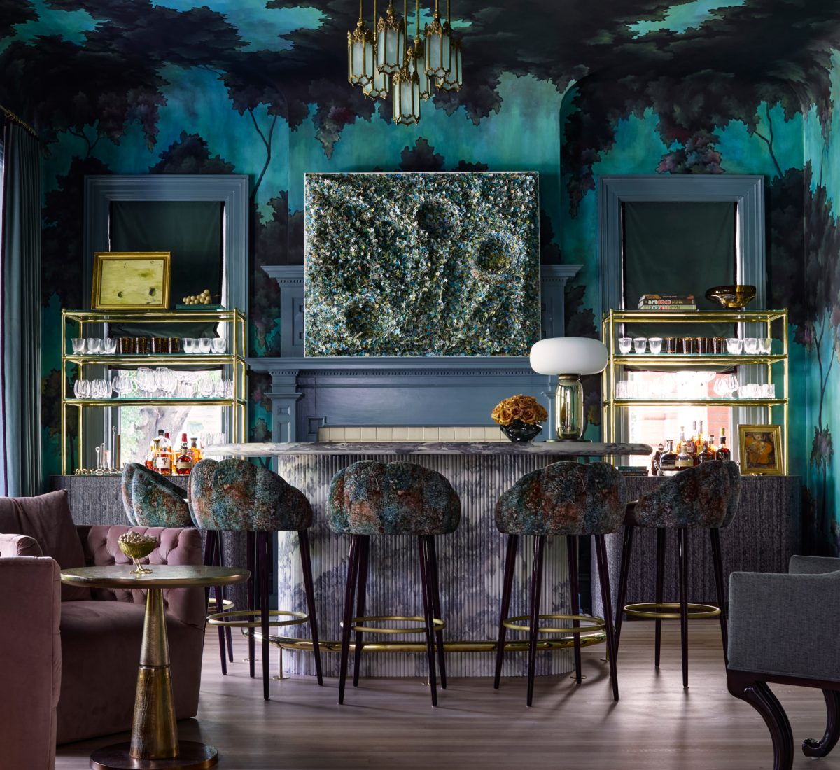 the bar of a house in Tampa Florida designed by Melanie Turner withturquoise and blue semi-gothic spanish moss hand0painted mural on walls and ceilings, marble clad bar with stools and pink chairs in foreground. fireplace behind bar flanked by windows