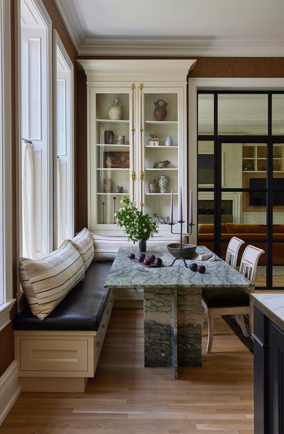 Directoire chairs tuck under the custom green-marble kitchen table opposite a built-in banquette with glass cabinets behind in the kitchen breakfast nook of a historic Chicago townhouse by design partners Laura Buxbaum Gordon and Nate Berkus