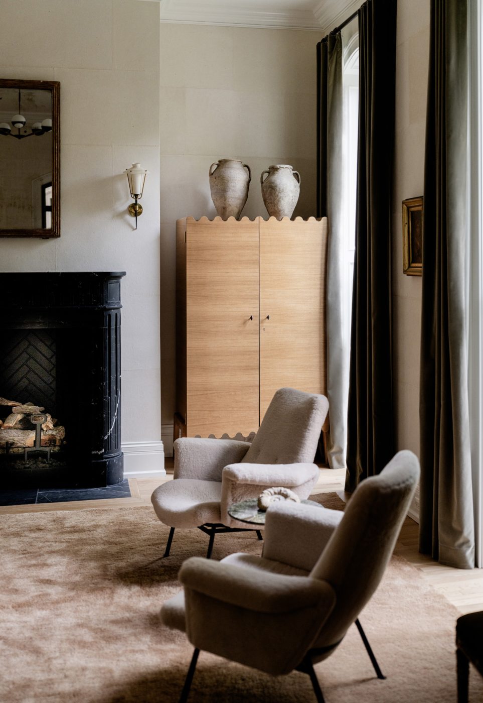 A pair of ca. 1950 Pierre Guariche armchairs sit between the fire place and tall windows in the living room of a historic Chicago townhouse by design partners Laura Buxbaum Gordon and Nate Berkus