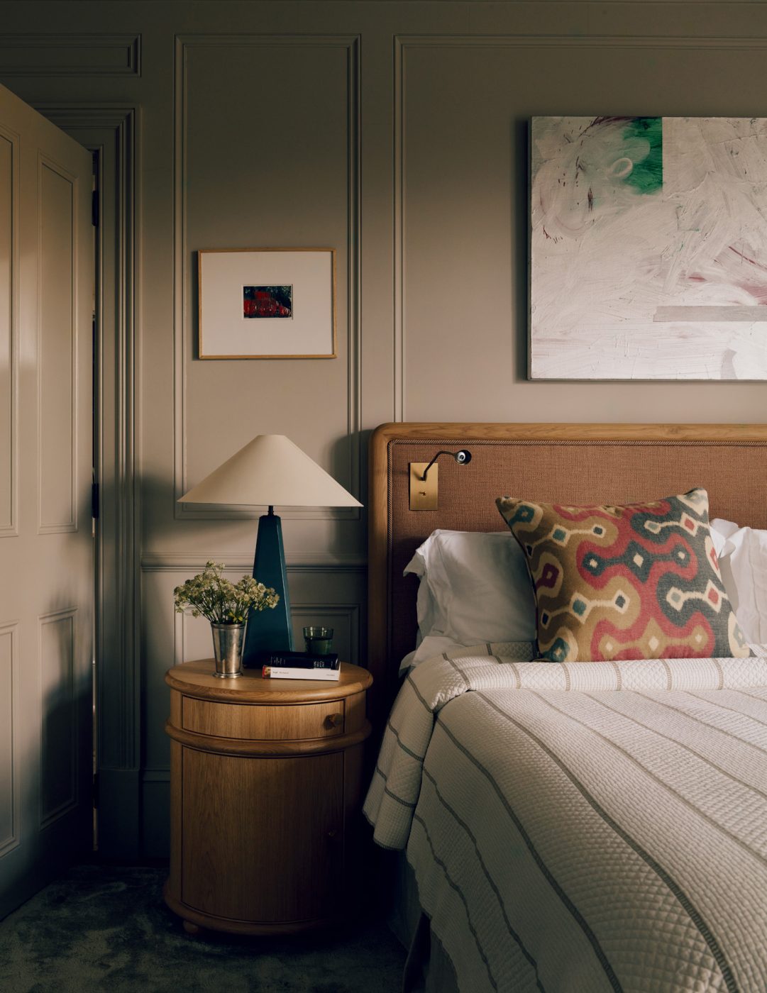 Primary bedroom of a Victorian townhouse in London's Holland Park designed by the studio De Rosee Sa and featuring a custom nightstand topped by a lamp from designer Susie Atkinson's London studio. The painting over the bed is by Jacqueline Humphries, and the piece over the lamp is by Gerhard Richter.