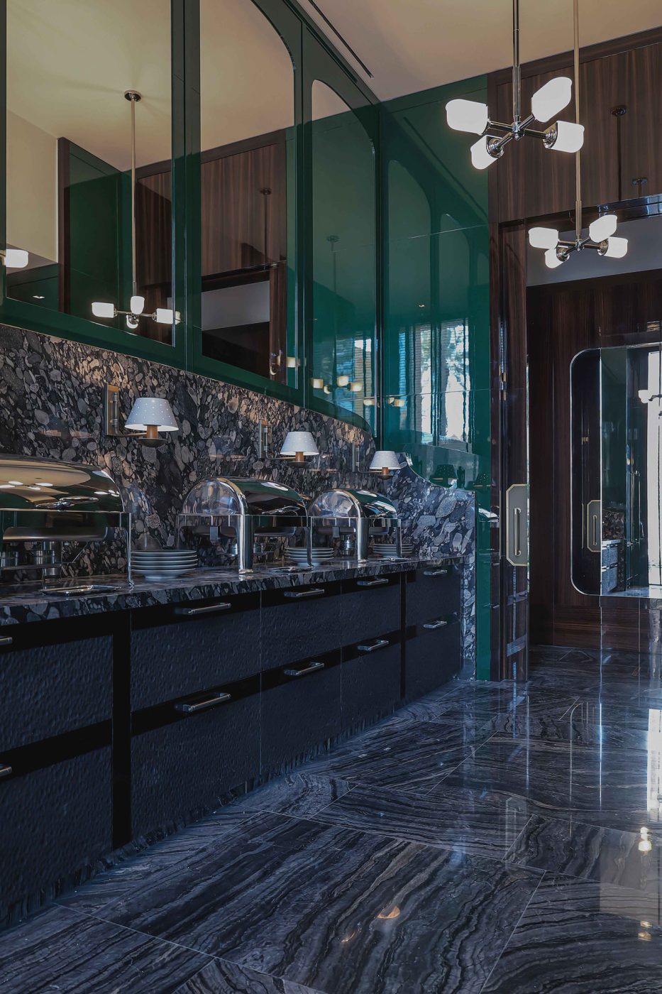 Roman and Williams pendants and Urban Electric Co. sconces in the stone clad green-painted cabinets kitchen of the entertaining pavilion on a large compound in Saudi Arabia by Jacques Bec and Artur Miranda's architecture and design studio Oitoemponto