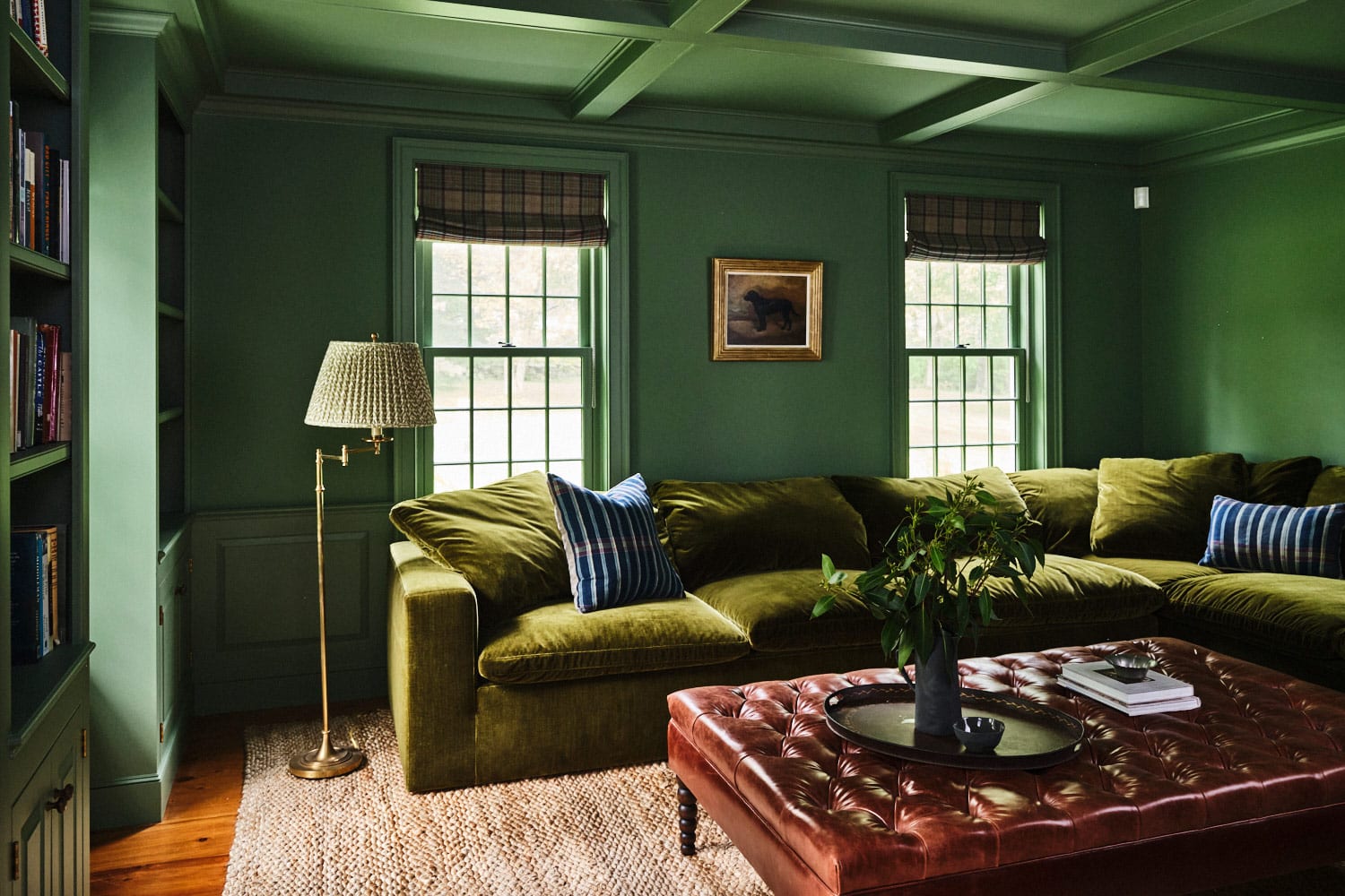 Library-turned-TV room of main house at Vermont countryside compound Sarah Shetter designed for Hollywood writer-producers featuring custom velvet sectional, button tufted brown leather ottoman used as cofeet abel and vintage floor lamp atop sisal/jute rug