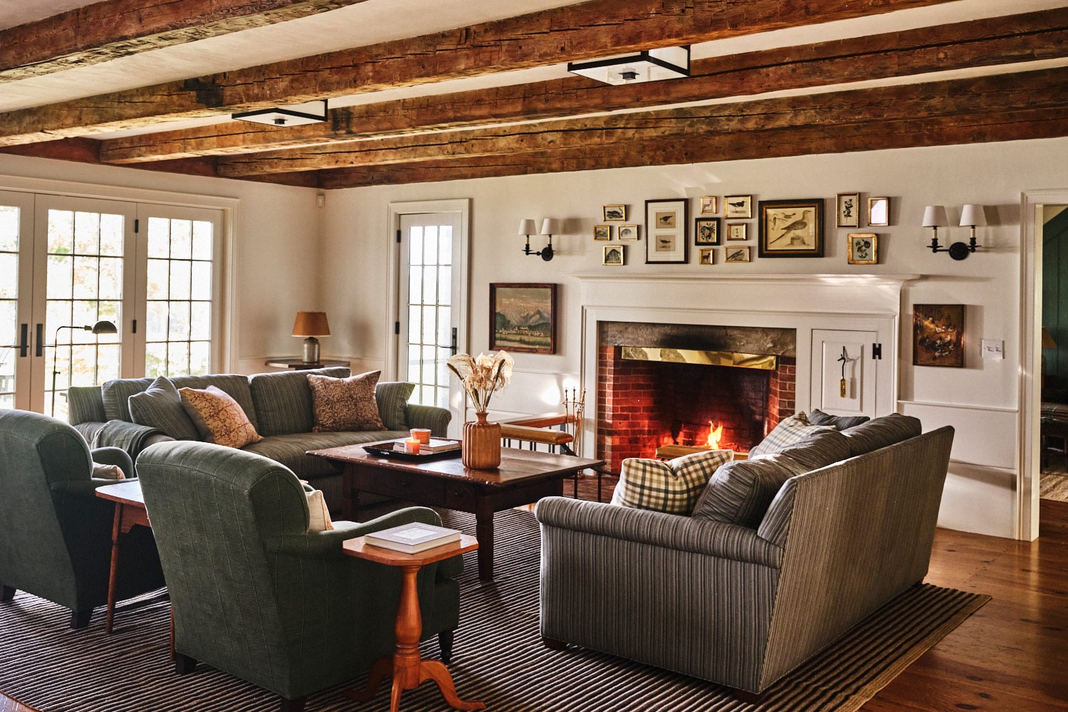 Family room of main house at Vermont countryside compound Sarah Shetter designed for Hollywood writer-producers. Includes a pair of striped sofas facing each other across a vintage ofee table and two armchairs facing fireplace all on a striped rug
