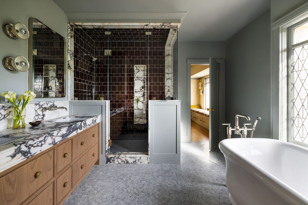 Primary bathroom of Craftsman-style house in San Francisco's Presidio designed by Katie Troutman with view into laundry room featuring leaded glass window, Water Monopoly tub, Urban Electric scounces, mosaic tile floors.